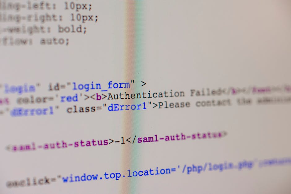 Close-up view of a MacBook Pro laptop screen displaying a code editor with colorful programming code on the left side, and a partially visible mobile phone on the right. The laptop is on a dark surfac