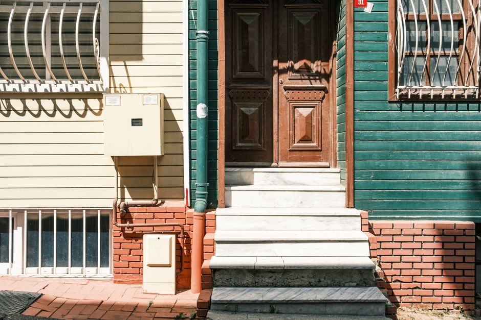 Detailed view of the entrance to a residential property showing a set of white marble steps leading up to a dark wooden front door with raised panels. To the left of the steps, there is a beige utilit